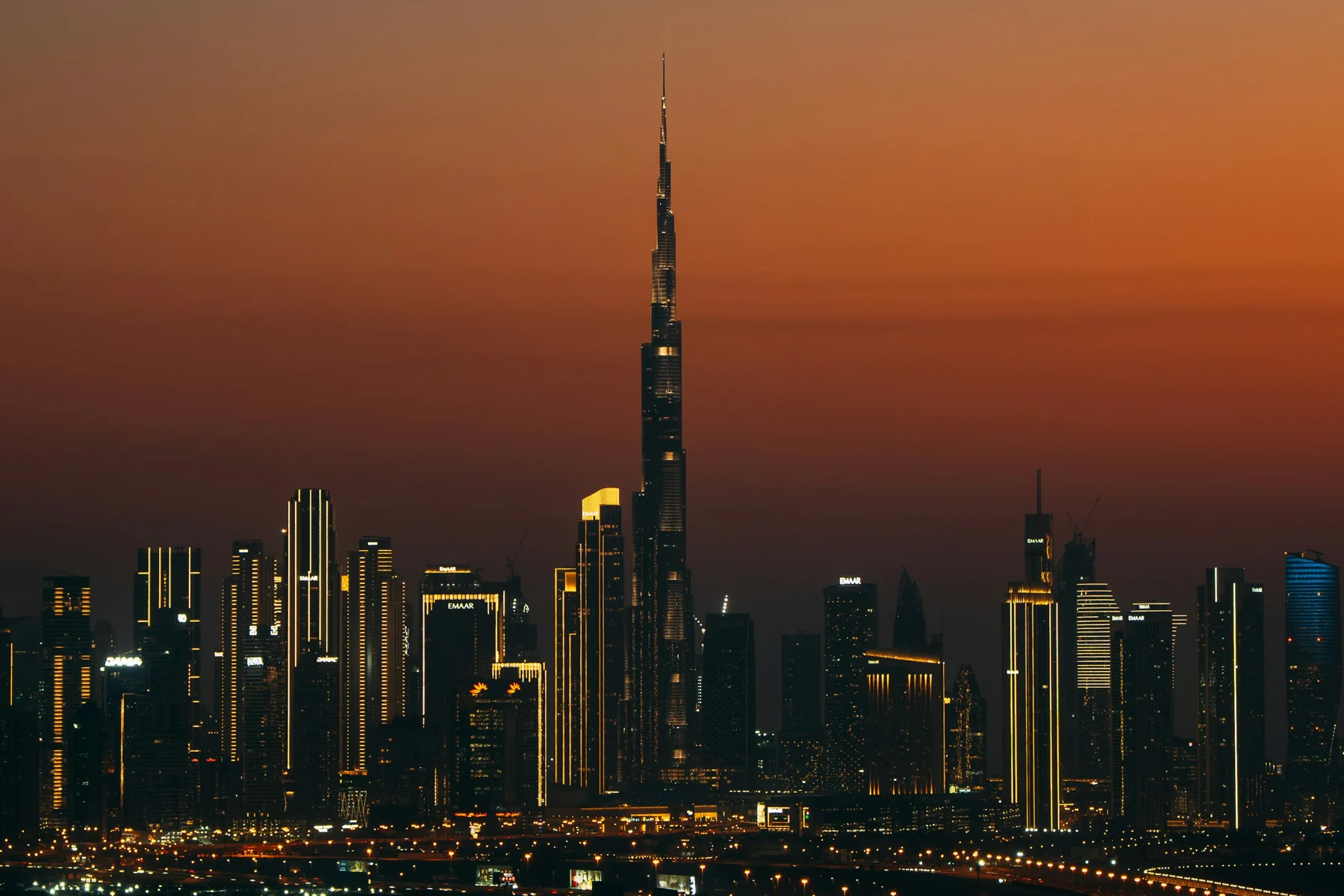 Burj Khalifa and the illuminated Downtown Dubai skyline beneath an orange dusk sky